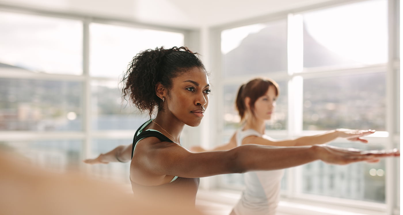 a woman in the foreground stretching her arms in a yoga pose with a woman in the background doing the same thing